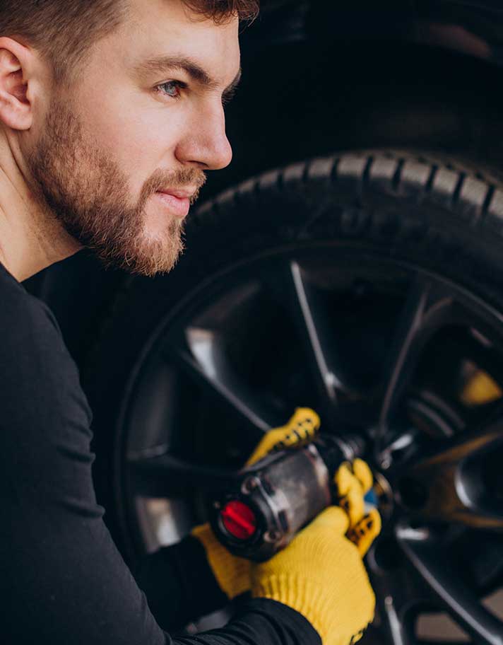 Mechanic adjusting the tires screw while facing side view.